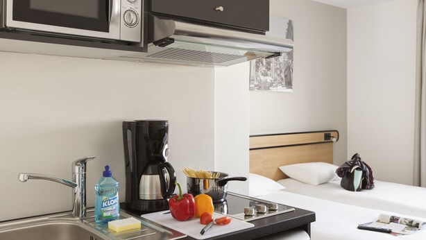 A compact hotel room with a kitchenette, a bed, a bedside table, and a window with a view. - Aparthotel Adagio Access Nancy Centre (Nancy)