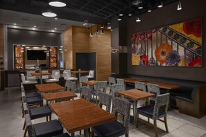 Un restaurante moderno con mesas y sillas de madera, una zona de bar y un gran mural floral en la pared.