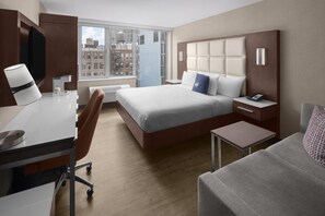 A modern hotel room with a large bed, a desk, a chair, a small table, and a sofa.