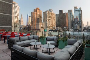 Eine Dachterrasse mit Außenmöbeln, Blick auf die Stadtlandschaft und moderne Gebäude im Hintergrund.
