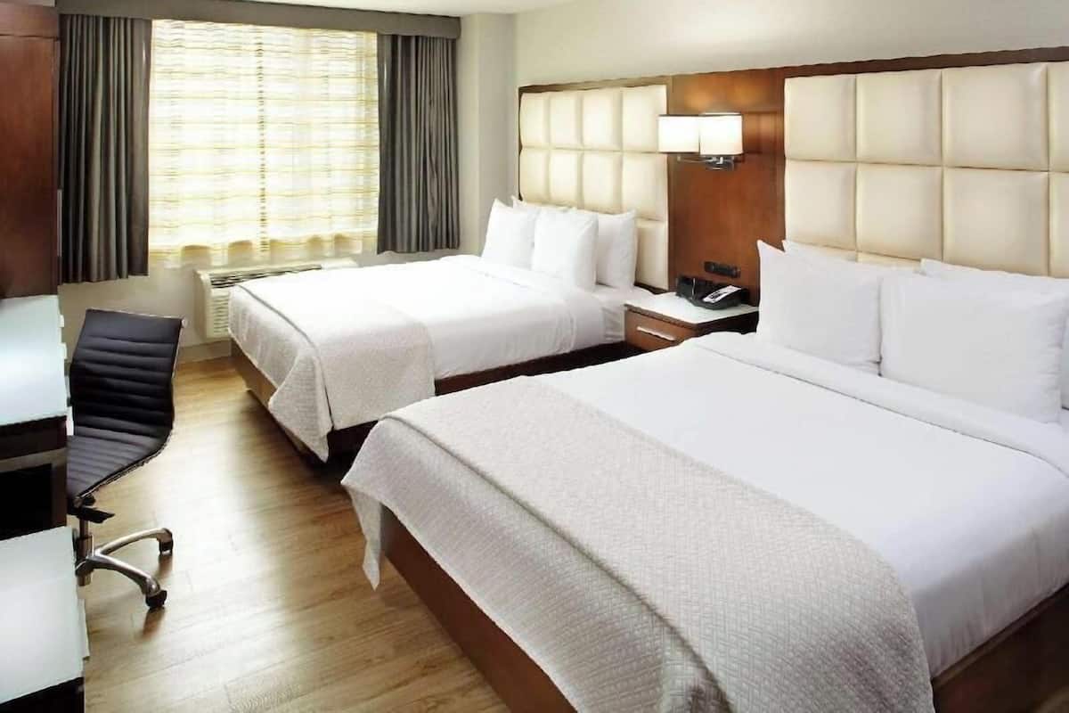 Habitación de hotel con dos camas, un escritorio, una silla y una ventana con cortinas.
