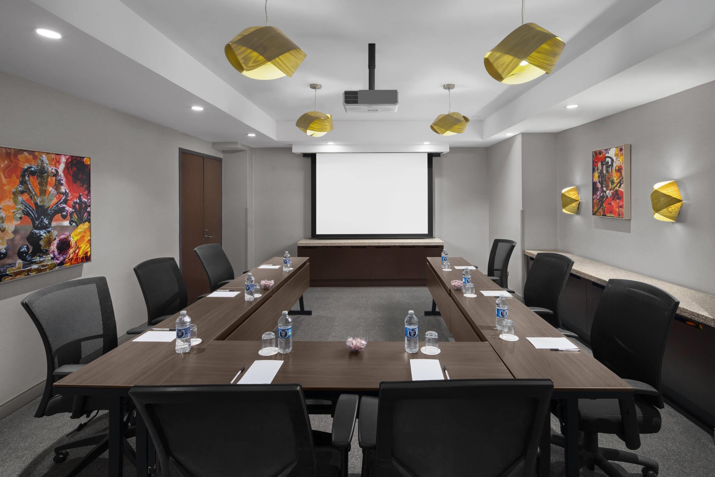 A conference room with a long table, chairs, a projector screen, and artwork on the walls.
