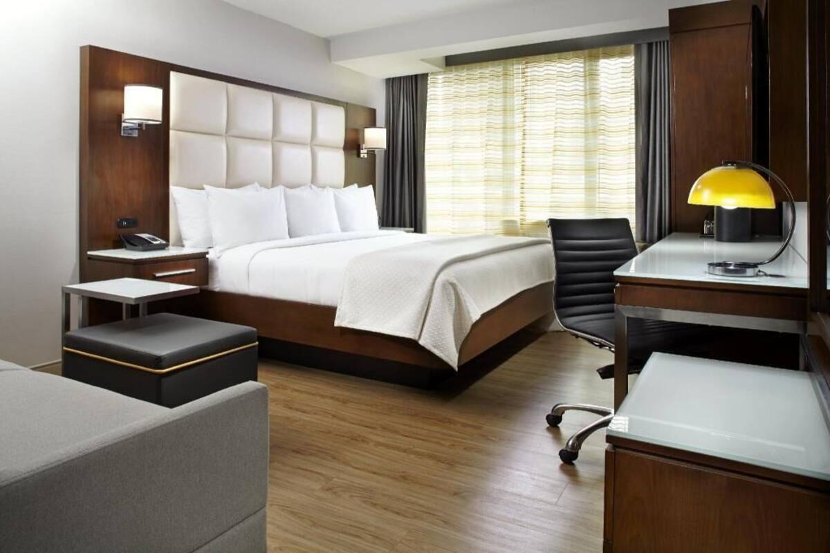 Una habitación de hotel con cama, mesitas de noche, escritorio, silla y lámpara.