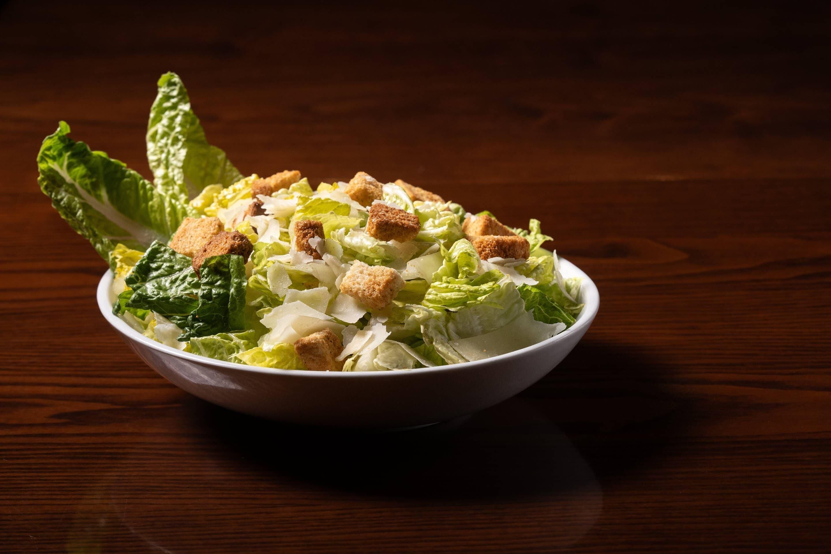 Un tazón de ensalada con crutones y lechuga sobre una mesa de madera.