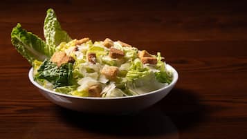 Un tazón de ensalada con crutones y lechuga sobre una mesa de madera.
