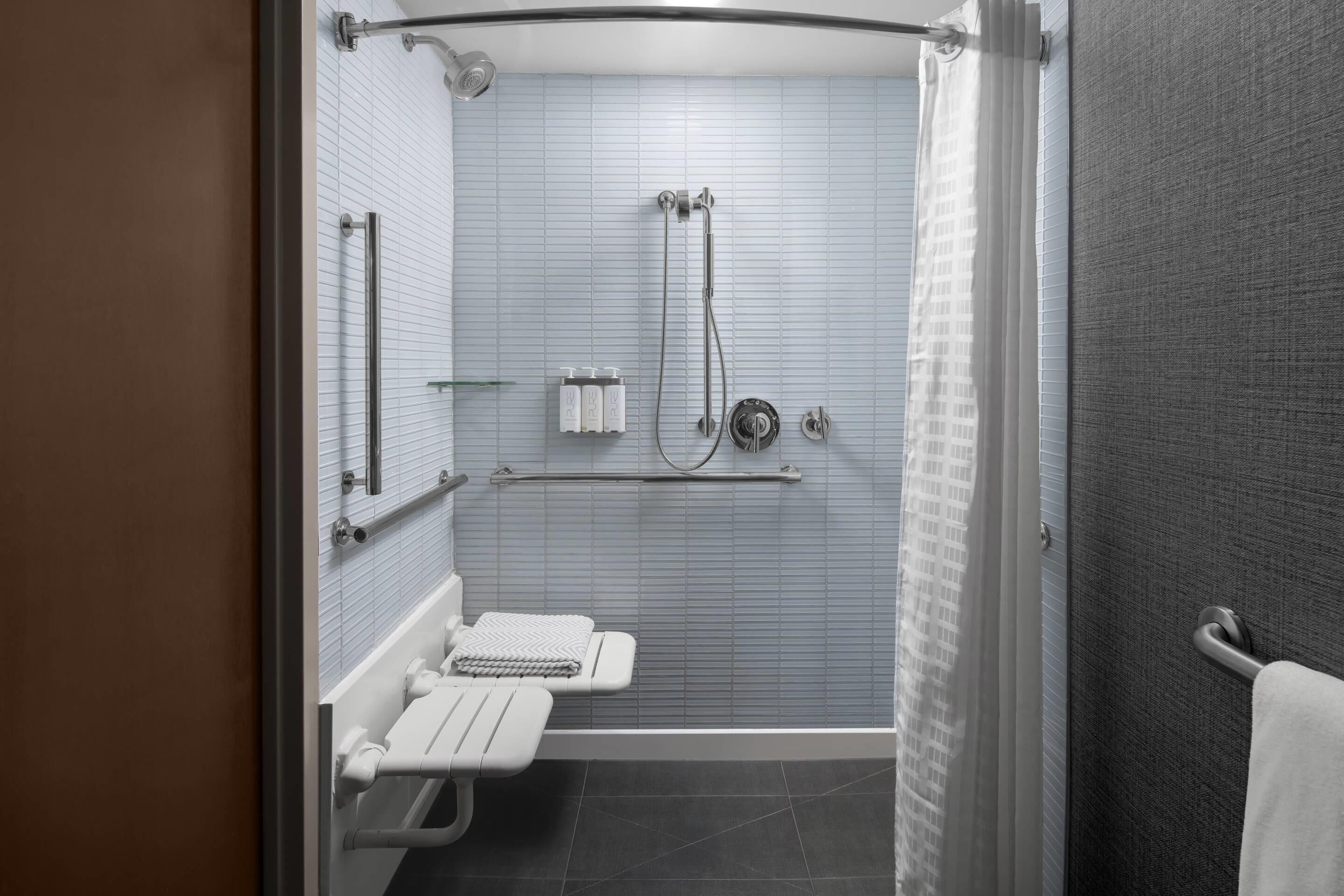 A modern bathroom with a shower, toilet, and grab bars.