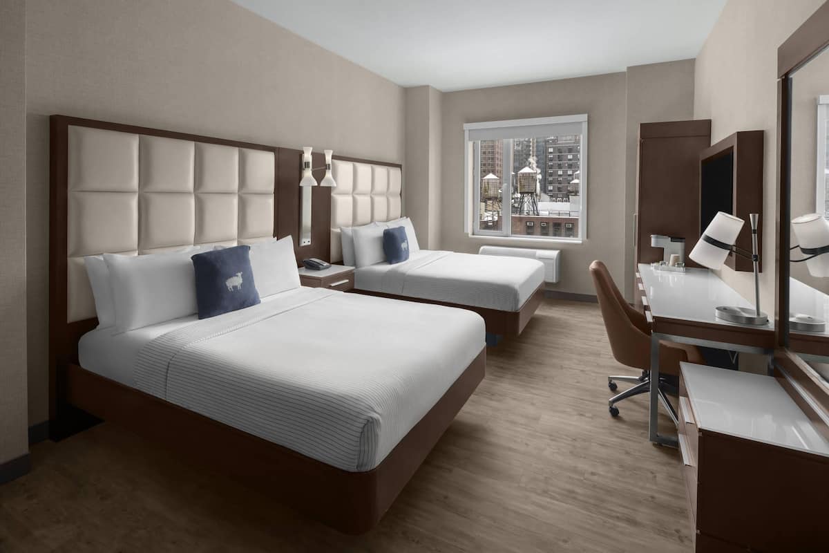 Habitación de hotel con dos camas, un escritorio y un ventanal grande con vistas a la ciudad.