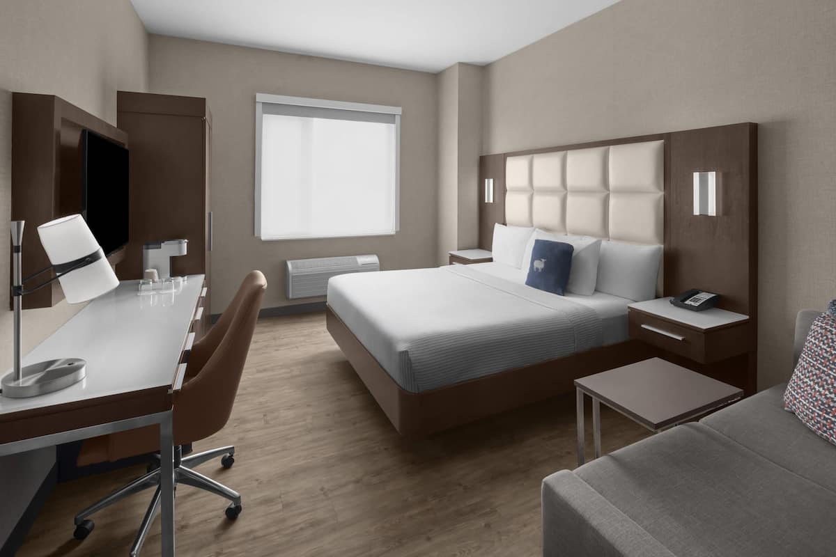 Una habitación de hotel moderna con una cama grande, un escritorio con una computadora, una silla y una mesita.