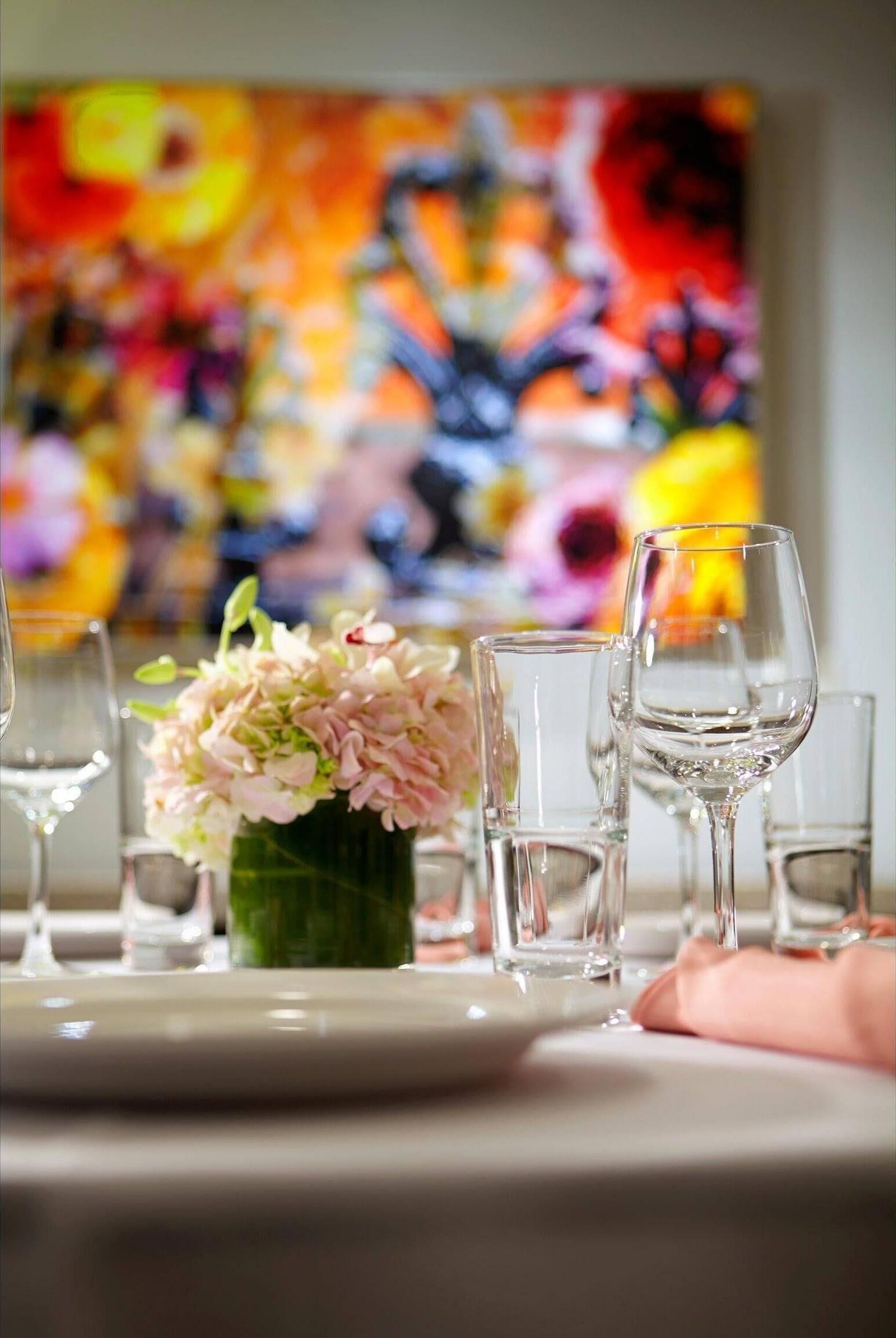 Una mesa de comedor con un jarrón de flores y varias copas de vino.