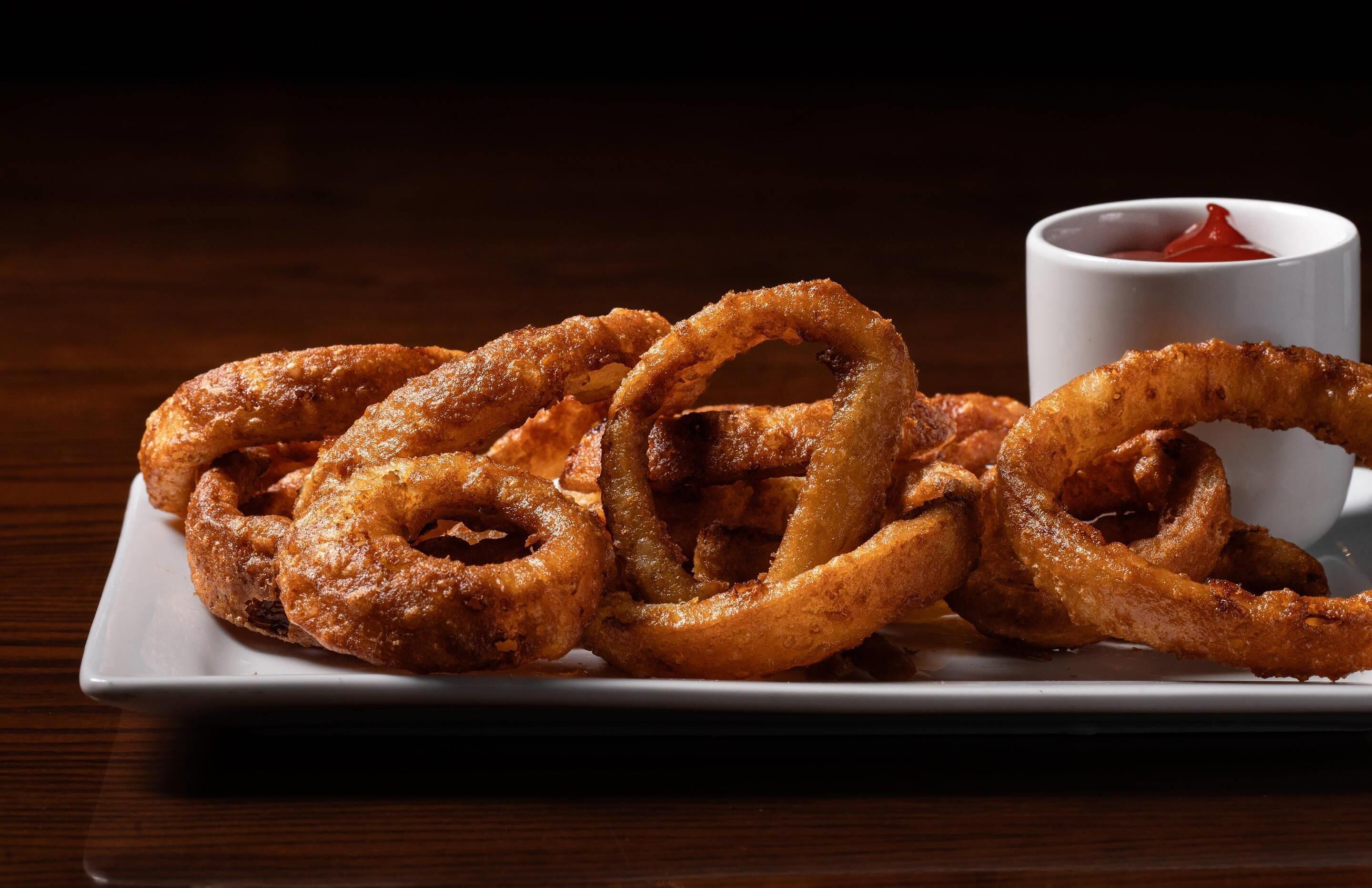 A plate of onion rings with a side of ketchup.