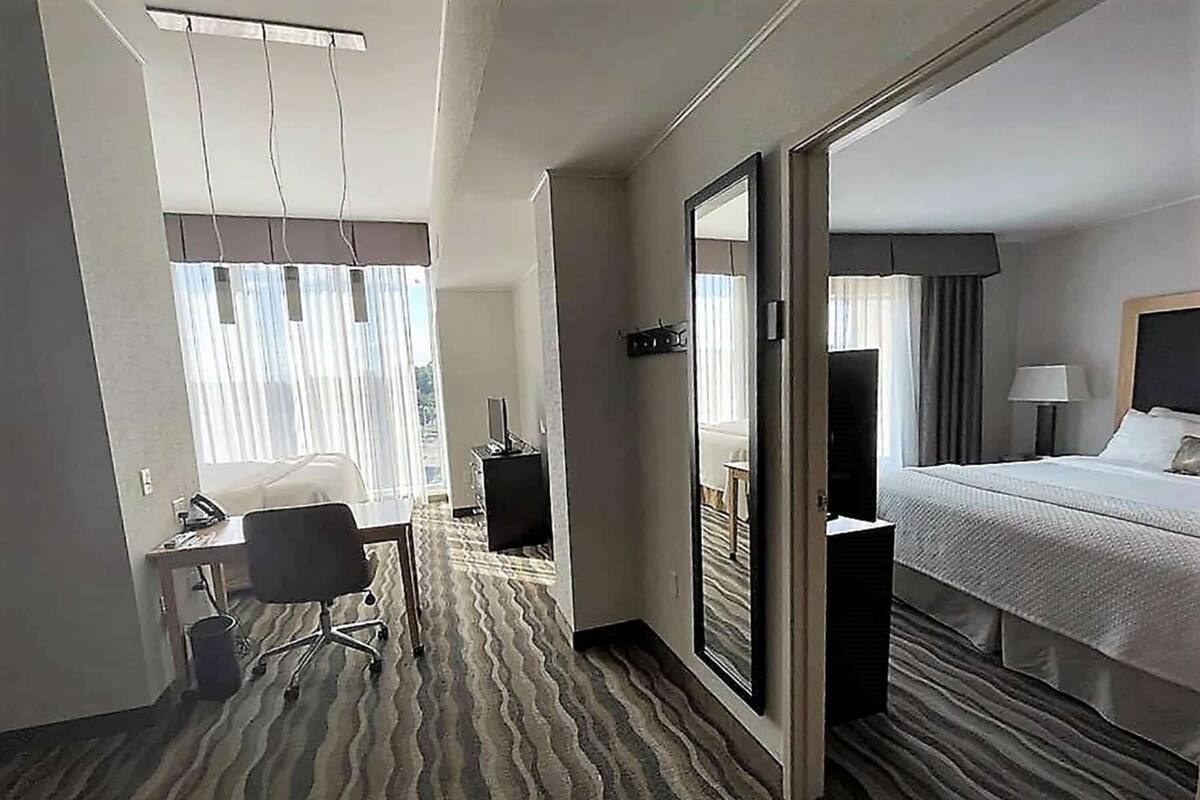 A hotel room with a bed, a desk with a chair, a mirror, and a window with curtains.
