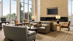 A spacious lobby with a large TV, comfortable seating, a fireplace, and large windows offering a view of the outdoors.