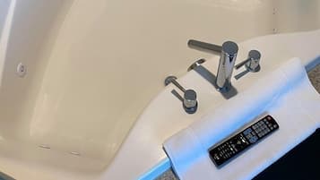 A white bathtub with a control panel and a remote control on a towel.