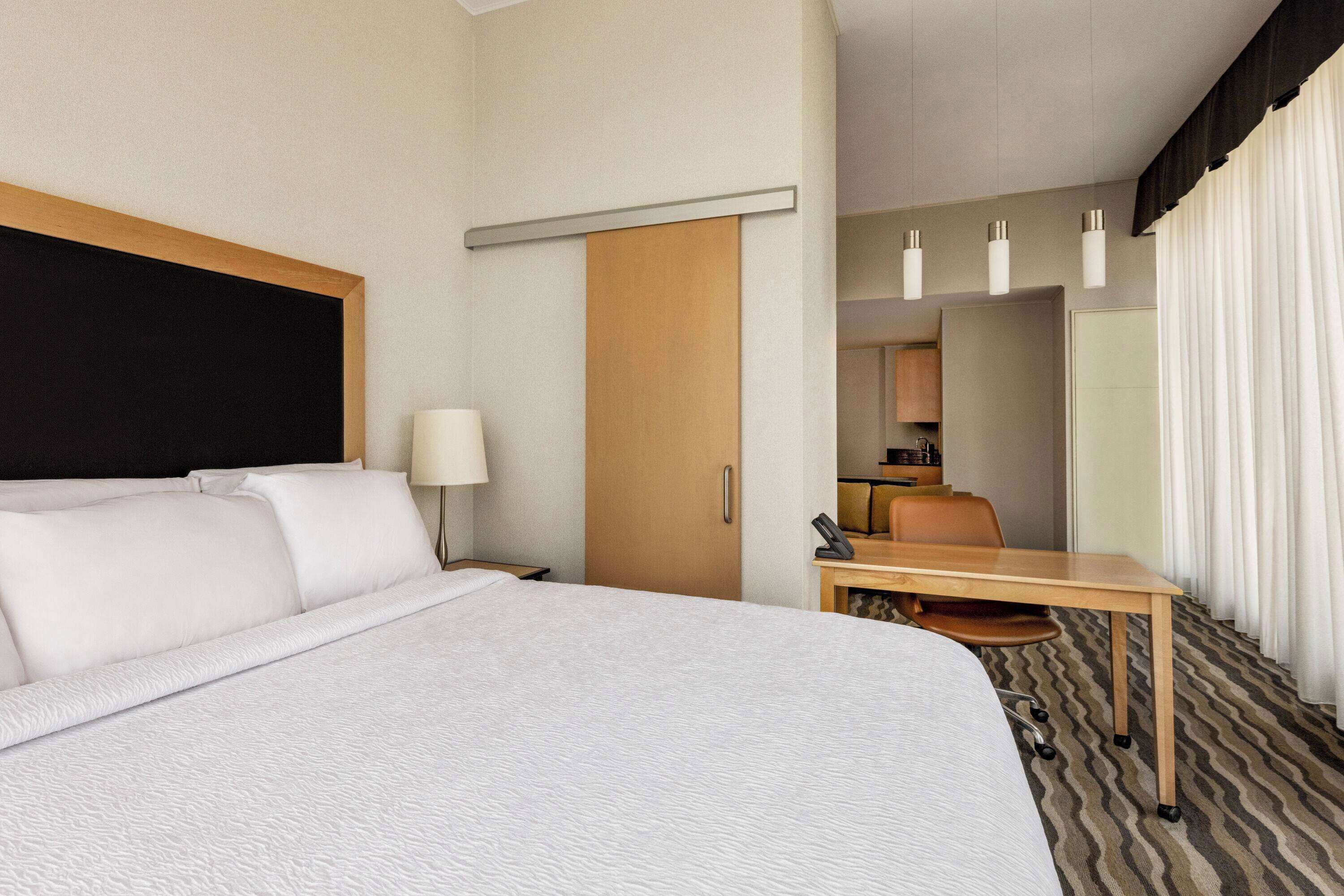 A hotel room with a large bed, a desk, a chair, a lamp, a telephone, and a mirror.