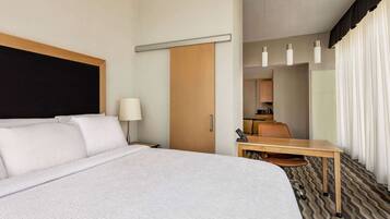 A hotel room with a large bed, a desk, a chair, a lamp, a telephone, and a mirror.