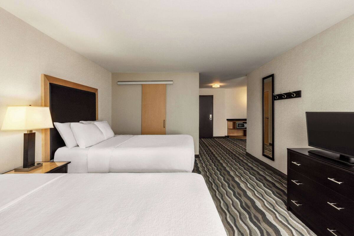 A hotel room with two beds, a TV, a dresser, and a bathroom visible in the background.