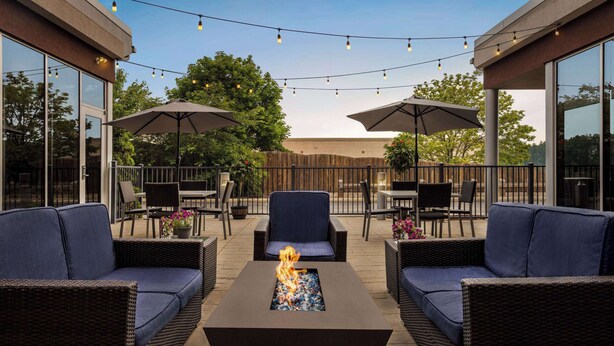 An outdoor patio area with wicker furniture, a central fire feature, and string lights.