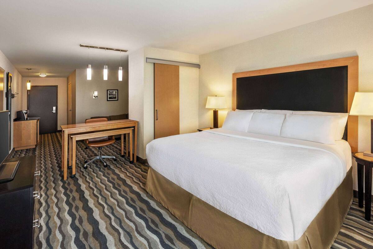 A hotel room with a large bed, a desk, a chair, a TV, and a door.