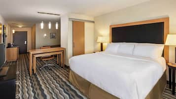 A hotel room with a large bed, a desk, a chair, a TV, and a door.