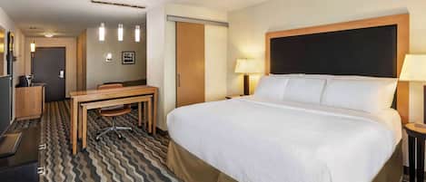 A hotel room with a large bed, a desk, a chair, a TV, and a door.