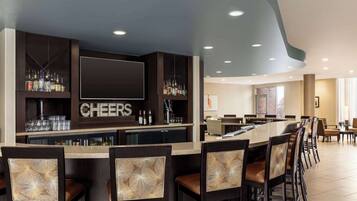 Eine Bar mit einer langen Theke, mehreren Sesseln und einem 'CHEERS'-Schild darüber.
