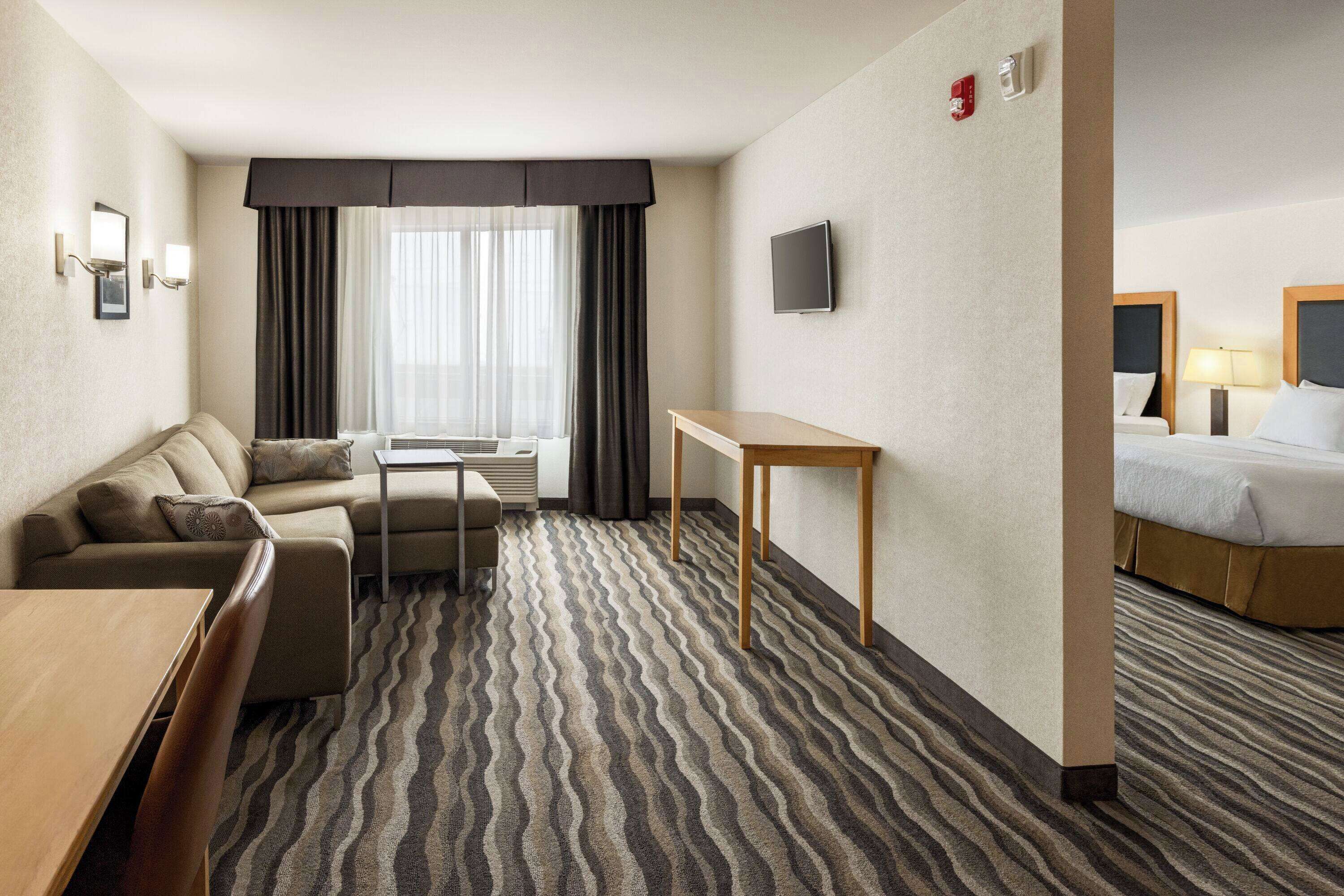 Hotellihuone, jossa on sohva, pieni pöytä, sänky ja ikkunasta avautuva näkymä ulos, ikkunassa on verhot.