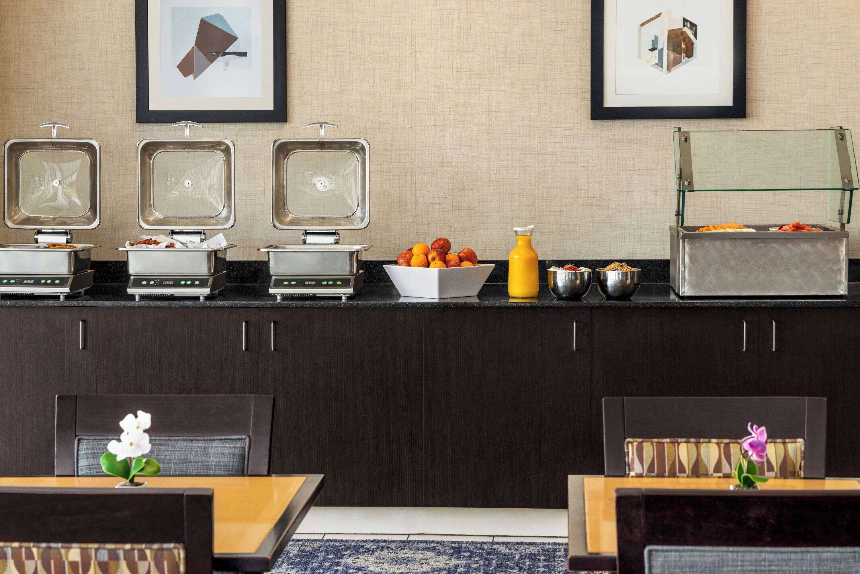 Un buffet pour le petit-déjeuner avec trois gaufriers, un saladier de fruits et un distributeur de jus.