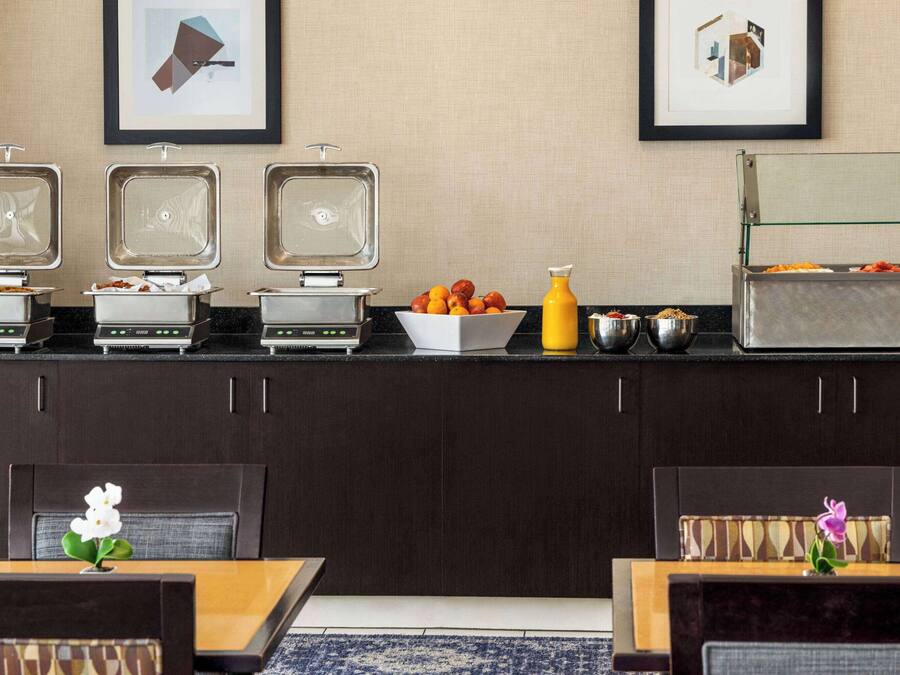 A breakfast bar with three waffle makers, a bowl of fruit, and a juice dispenser.