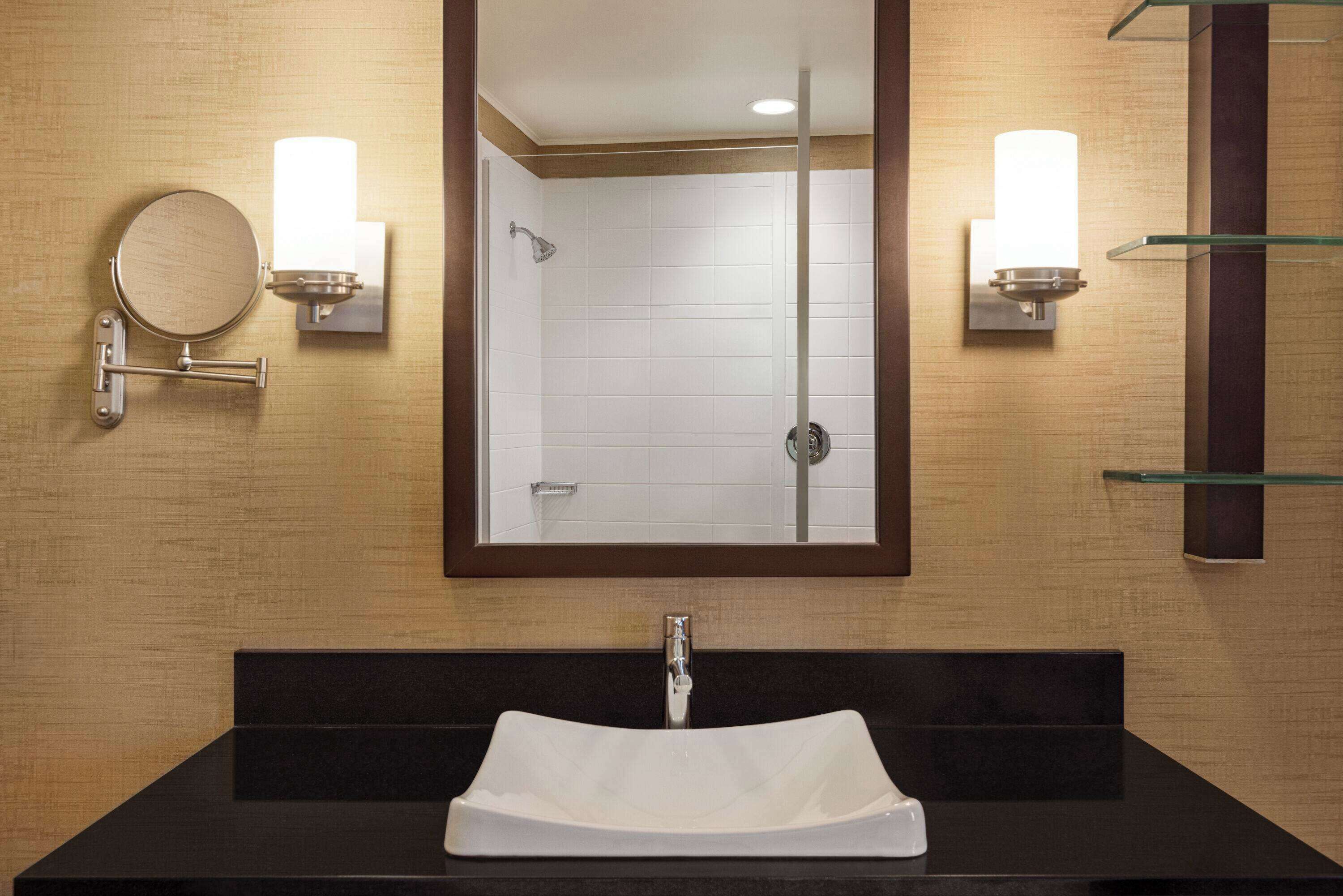 A bathroom with a large mirror, a white sink, and two wall-mounted light fixtures.