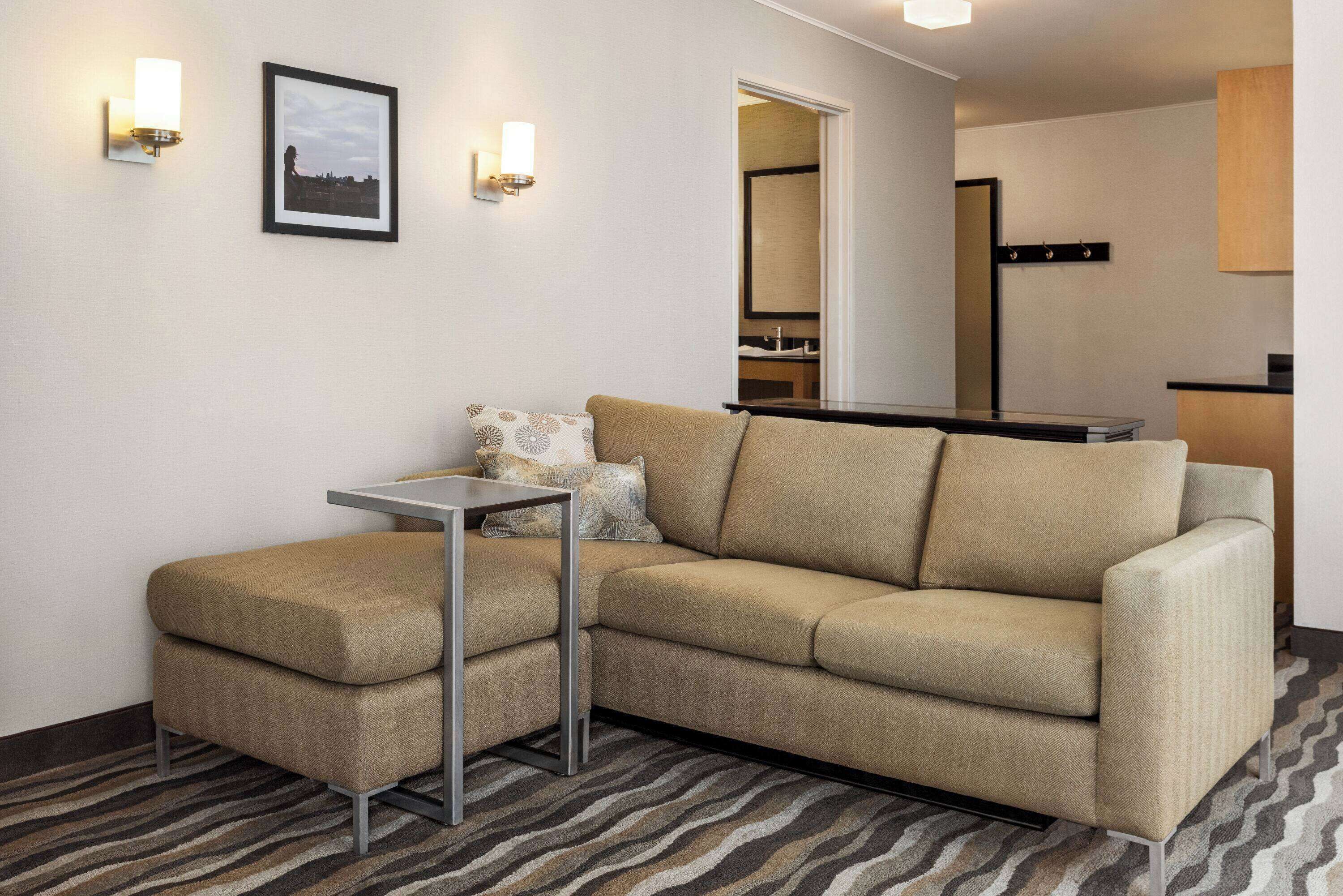 A modern living room with a sectional sofa, a small table, and two wall-mounted light fixtures.