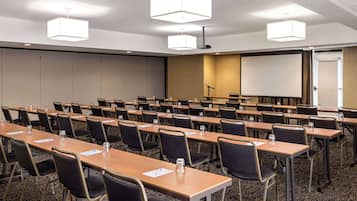 Un salón de conferencias con varias mesas y sillas, equipado con botellas de agua y blocs de notas.