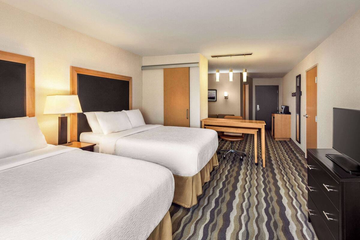 A hotel room with two beds, a desk, a television, and a bathroom visible through an open door.