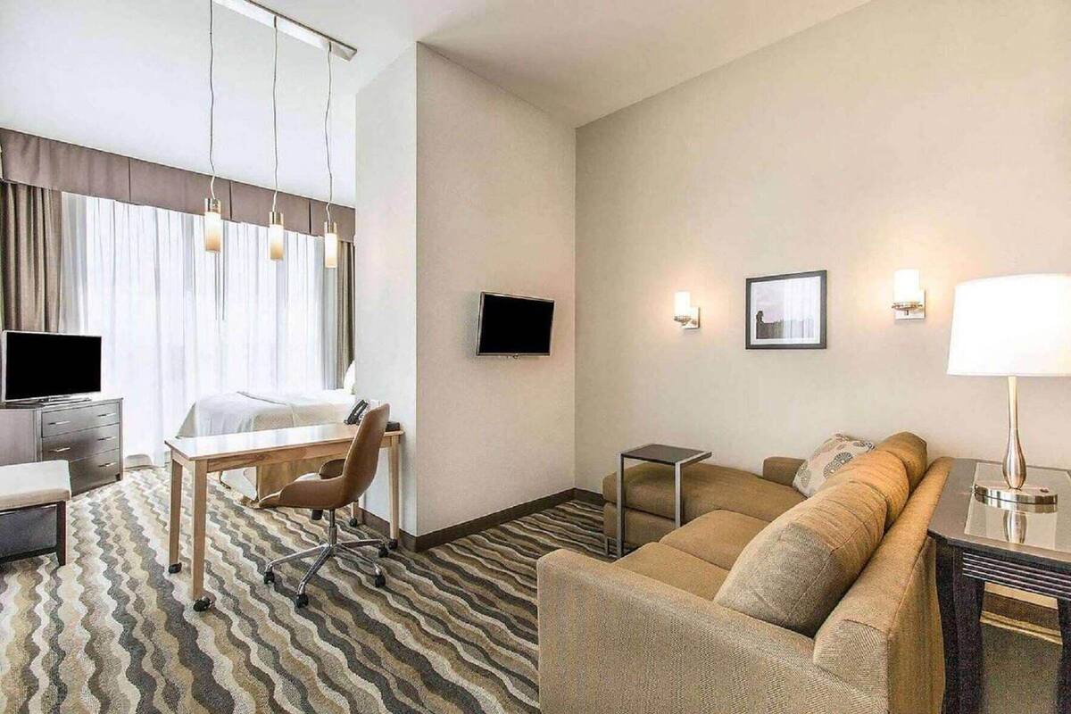 A hotel room with a bed, a desk with a chair, a sofa, a TV, and a lamp.