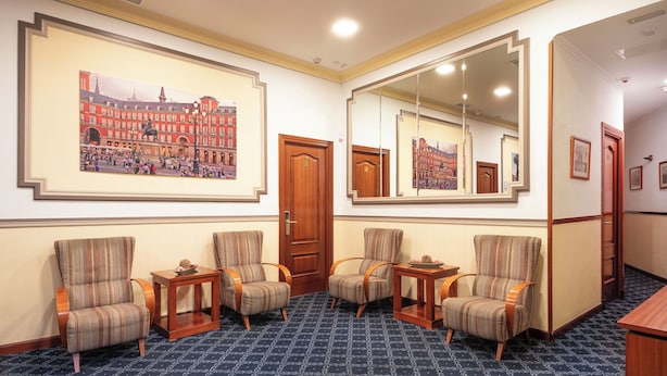 A hotel lobby with striped armchairs, a large mirror, and a framed cityscape painting on the wall. - Hostal Edreira (Madrid)