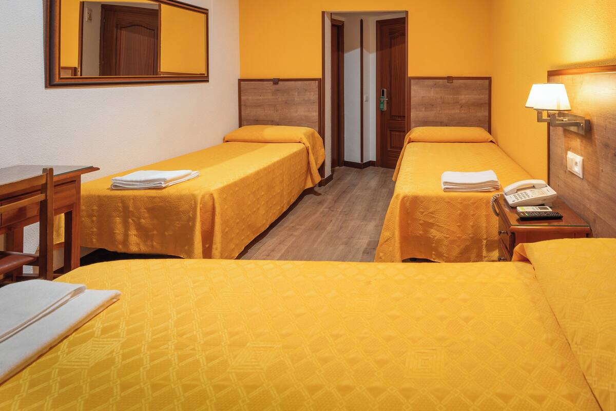 A hotel room with two single beds, a desk, a chair, a telephone, and a lamp.
