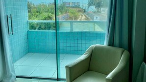 A room with a sliding glass door leading to a balcony, a beige armchair, and tiled walls. - Hotel Adventure (São Luís)