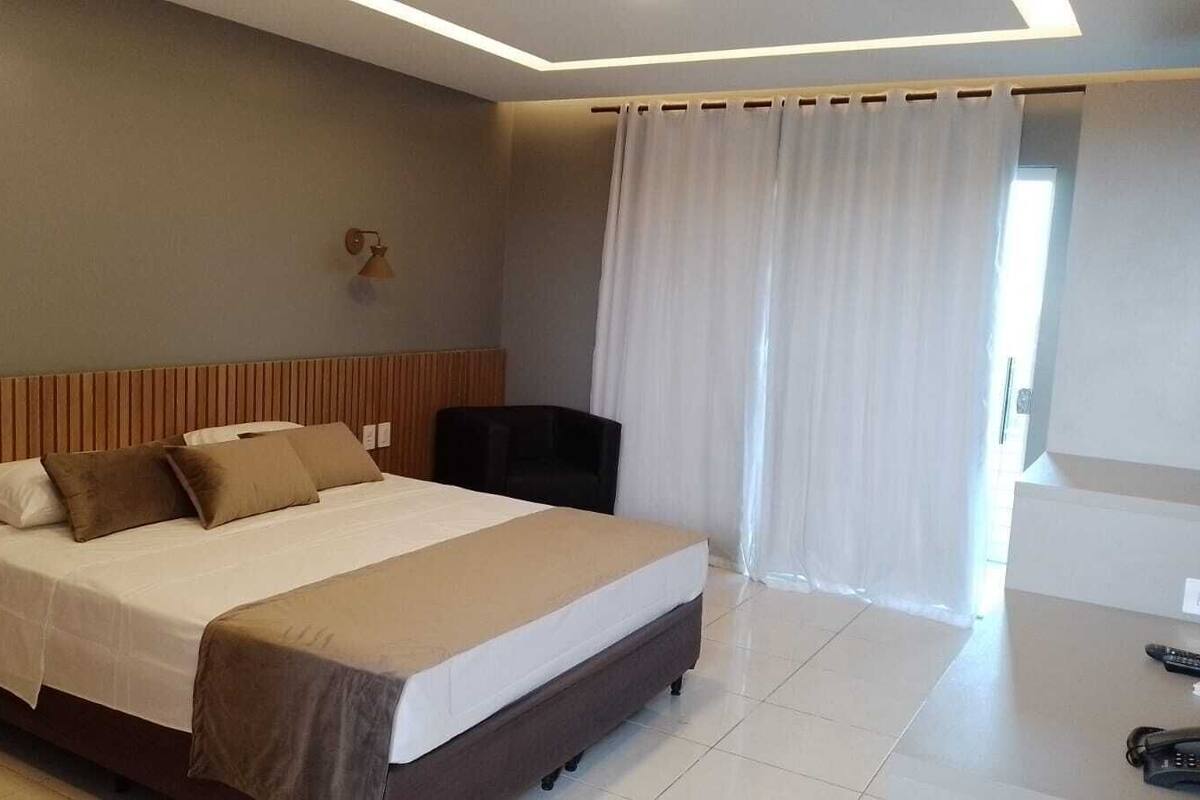 A hotel room with a bed, a desk, a chair, and a window with curtains.