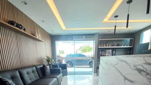 A modern lobby with a black leather sofa, a marble reception desk, and a view of the street outside. - Hotel Adventure (São Luís)