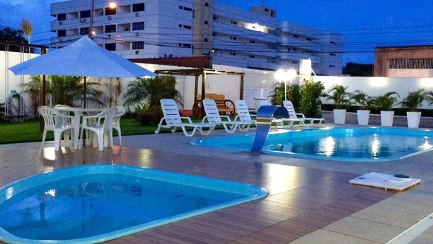 A swimming pool area with lounge chairs and umbrellas, surrounded by a wooden deck and potted plants. - Hotel Adventure (São Luís)