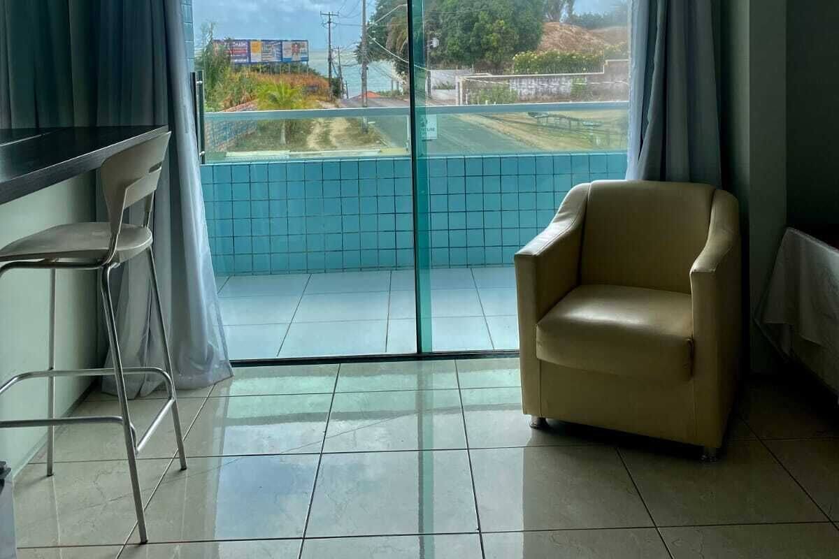 A room with a sliding glass door leading to a balcony, a chair, a small table, and a bar area.