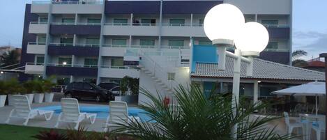 Un hotel con piscina, zona de estar al aire libre y una gran estructura iluminada.