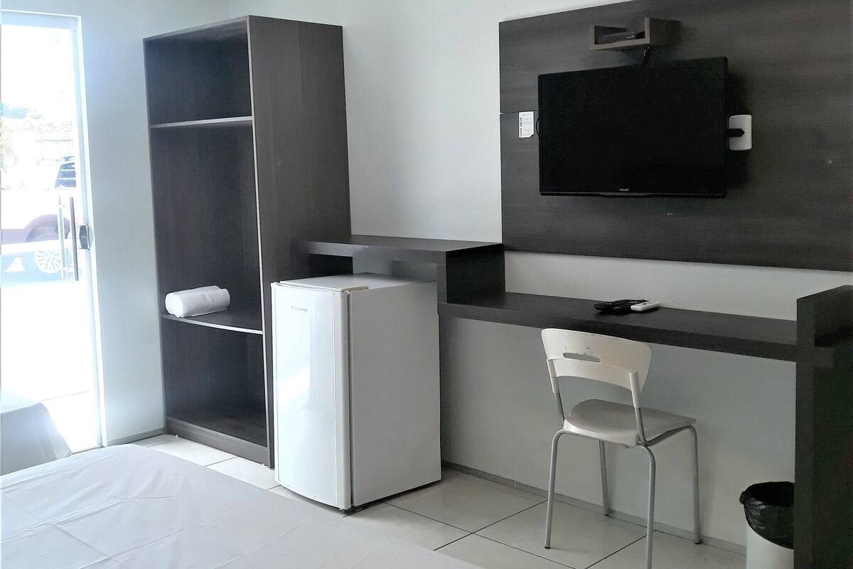 A hotel room with a bed, a desk, a chair, a TV, a refrigerator, and a wardrobe.