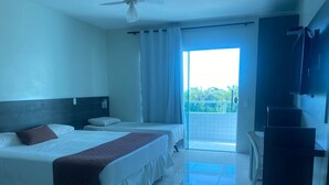 A hotel room with two beds, a ceiling fan, a TV, and a balcony with a view of greenery. - Hotel Adventure (São Luís)