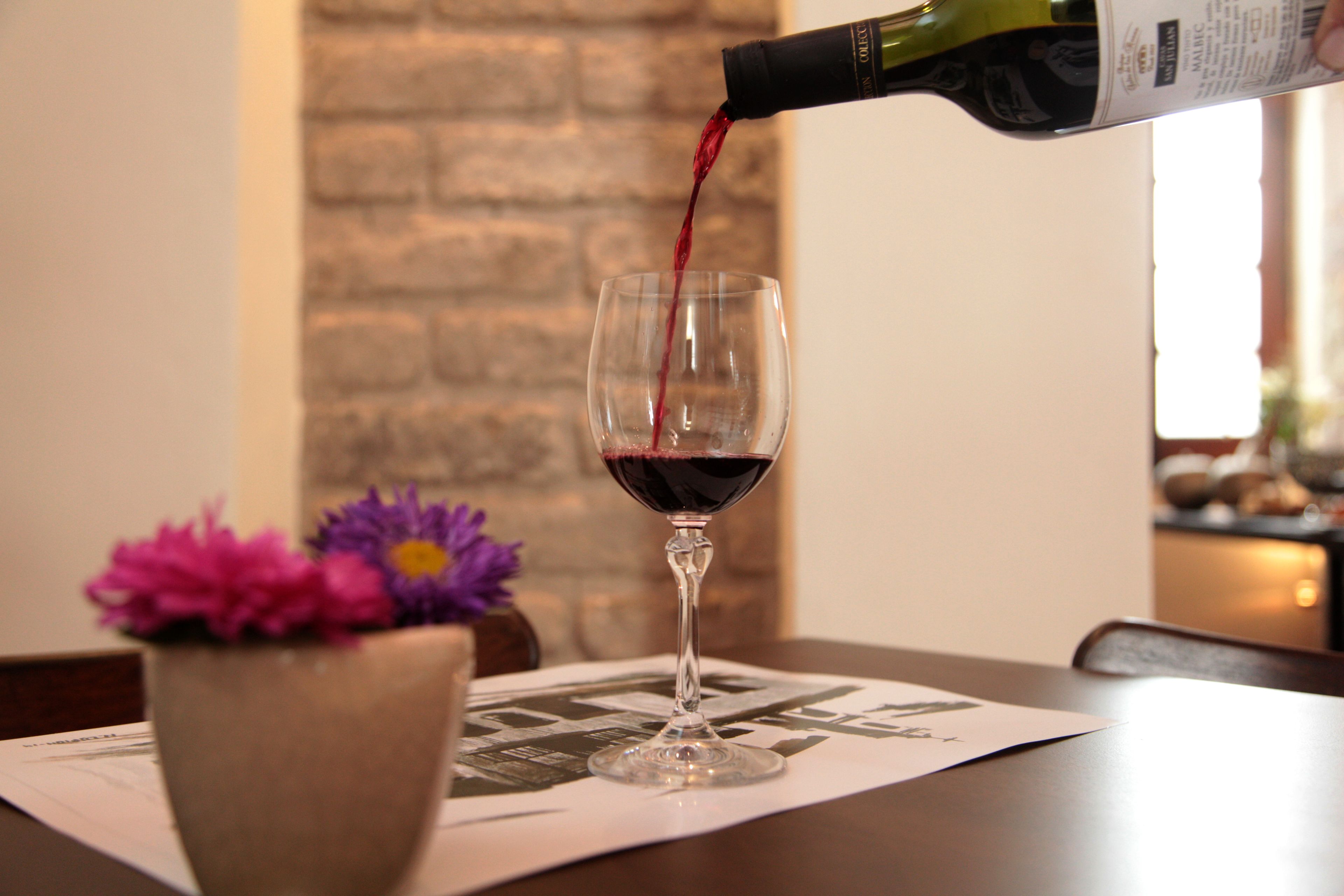 A wine glass being filled with red wine on a table with a brick wall in the background.