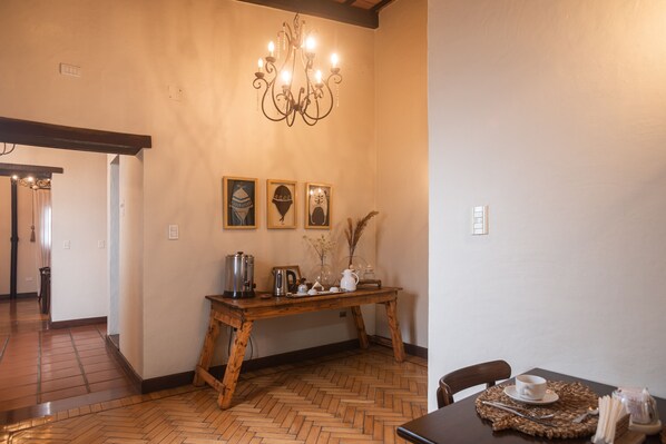 A wooden dining table with a placemat, a coffee pot, and a vase with dried plants. - Balcón de la Plaza (Salta)