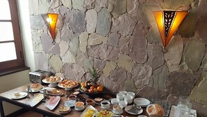 Un buffet per la colazione con diversi cibi e bevande, con sullo sfondo un muro in pietra e due luci a parete.