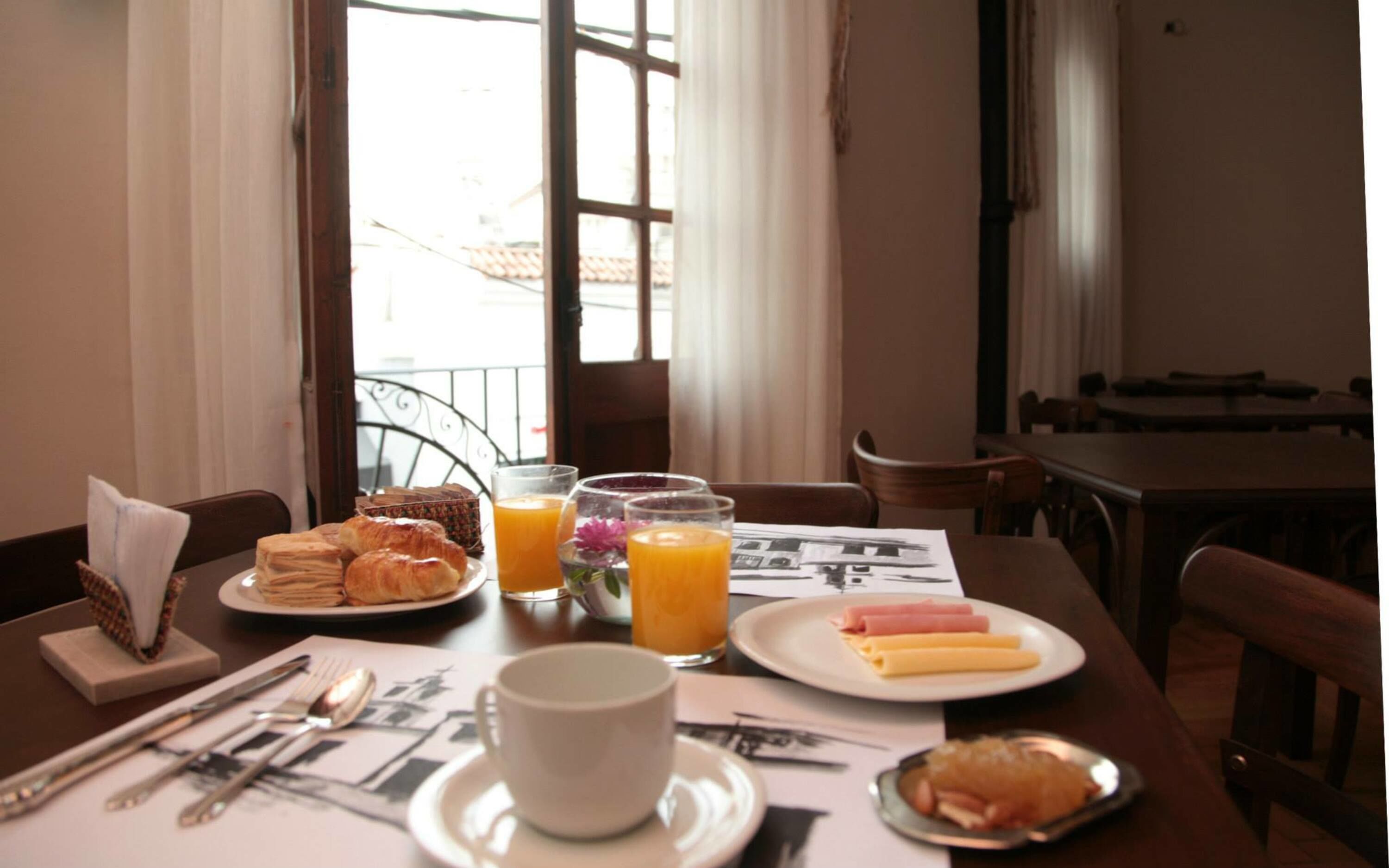 A breakfast table with croissants, ham, cheese, and orange juice.