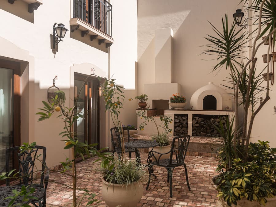 A courtyard with a brick floor, potted plants, outdoor furniture, and a fireplace.