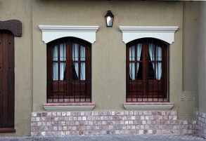 Facciata di un edificio con due finestre ad arco, un piccolo balcone e un fioriera luminosa a parete.