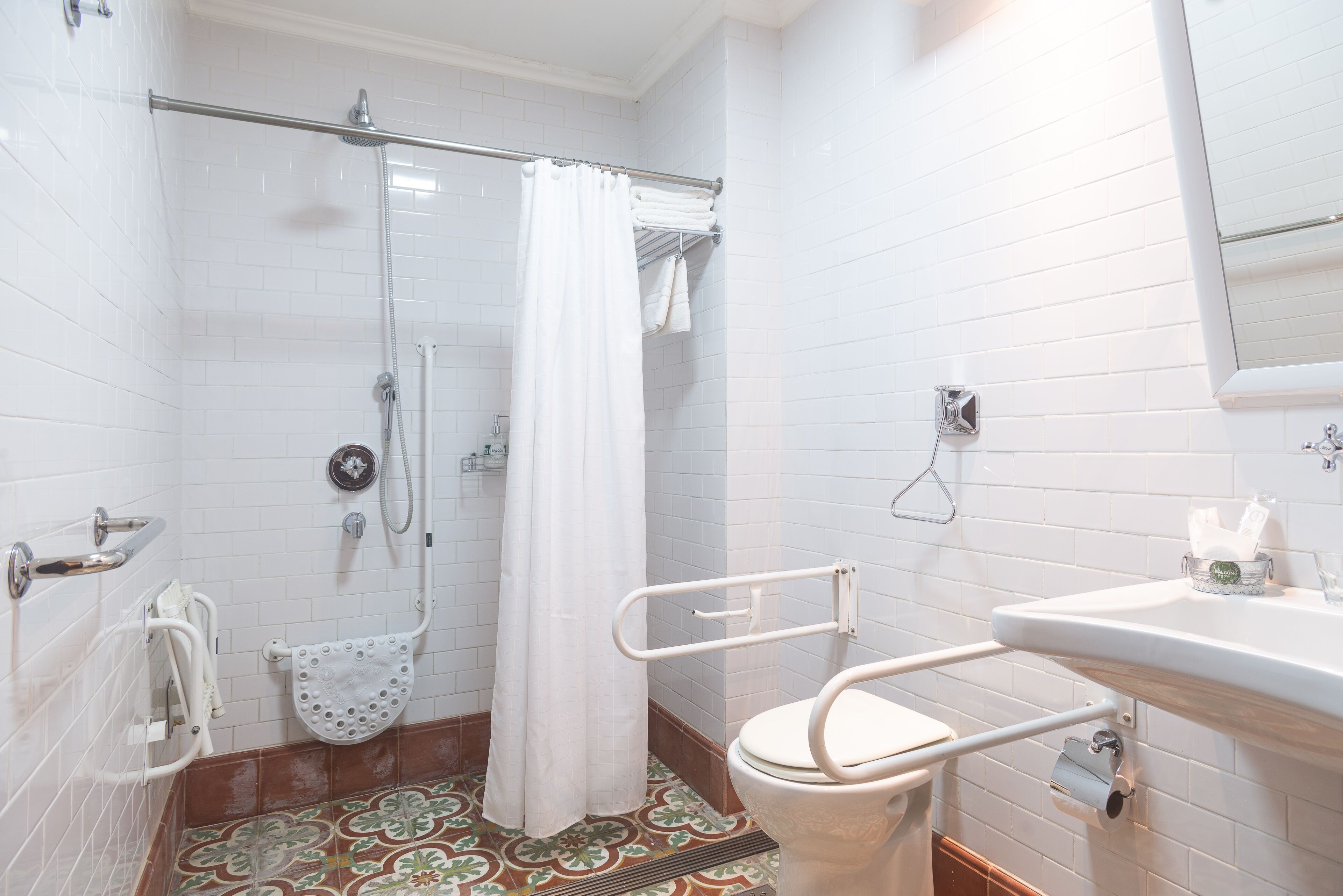 Een badkamer met witte betegelde wanden, een douche met glazen deur, een toilet met een veiligheidsbeugel en een wastafel met spiegel erboven.
